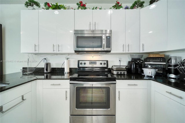 kitchen featuring appliances with stainless steel finishes, dark stone countertops, and white cabinetry