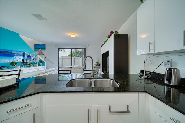 kitchen featuring sink, dark stone countertops, and white cabinetry