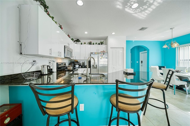 kitchen featuring appliances with stainless steel finishes, light tile floors, white cabinets, tasteful backsplash, and pendant lighting