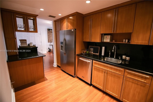 kitchen with light hardwood / wood-style flooring, dark stone counters, stainless steel appliances, and sink