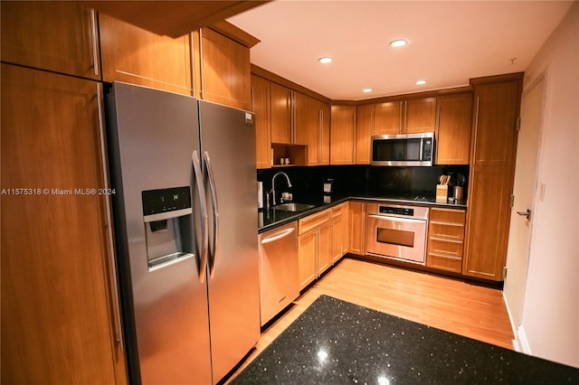 kitchen with stainless steel appliances, tasteful backsplash, dark stone countertops, sink, and light wood-type flooring