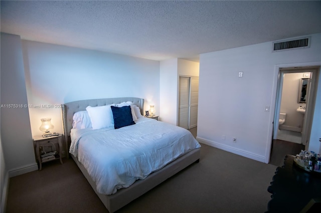 bedroom featuring a closet, a textured ceiling, dark colored carpet, and connected bathroom