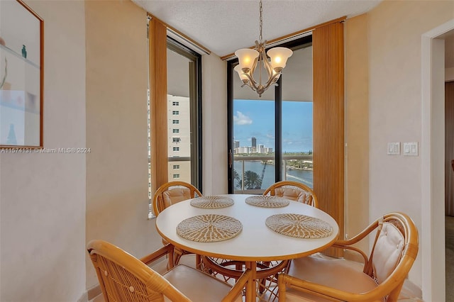 dining space featuring a wall of windows, a notable chandelier, a water view, and a textured ceiling