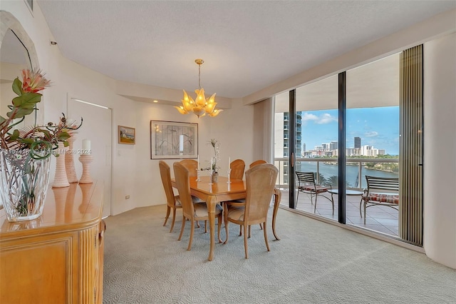 carpeted dining room featuring a textured ceiling, a notable chandelier, and a water view