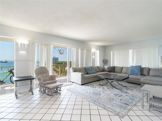 living room with a water view, a textured ceiling, and light tile patterned floors