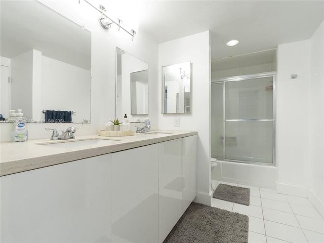 full bathroom featuring double vanity, toilet, shower / bath combination with glass door, tile patterned floors, and a sink