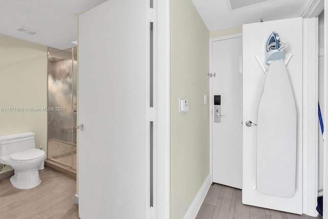 bathroom with an enclosed shower, toilet, and wood-type flooring