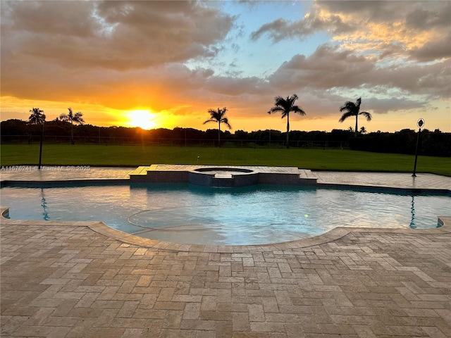 pool at dusk with an in ground hot tub and a yard