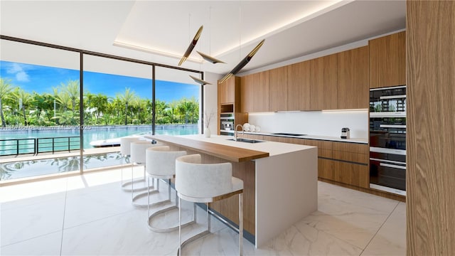 kitchen featuring sink, a breakfast bar area, black electric stovetop, a water view, and a center island with sink