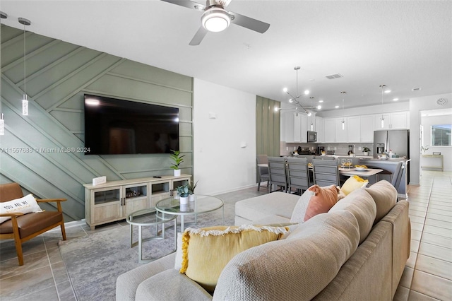 tiled living room featuring ceiling fan with notable chandelier