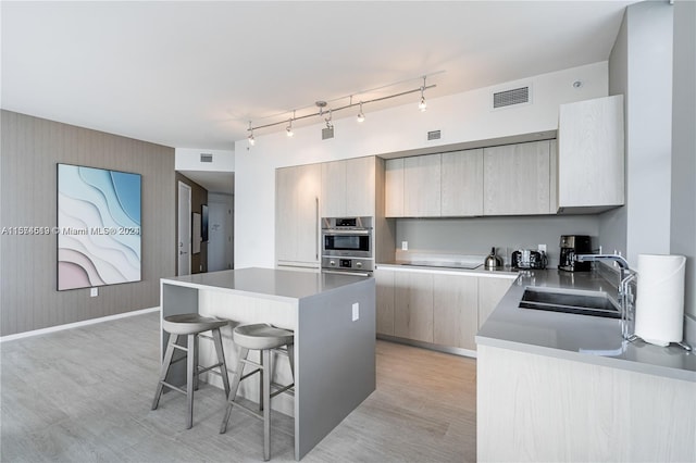 kitchen with a kitchen breakfast bar, light wood-type flooring, track lighting, a center island, and sink