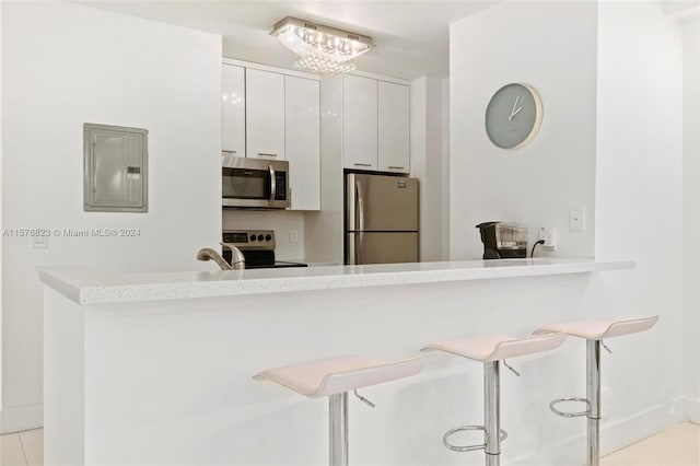 kitchen with white cabinets, stainless steel appliances, light tile floors, and a breakfast bar