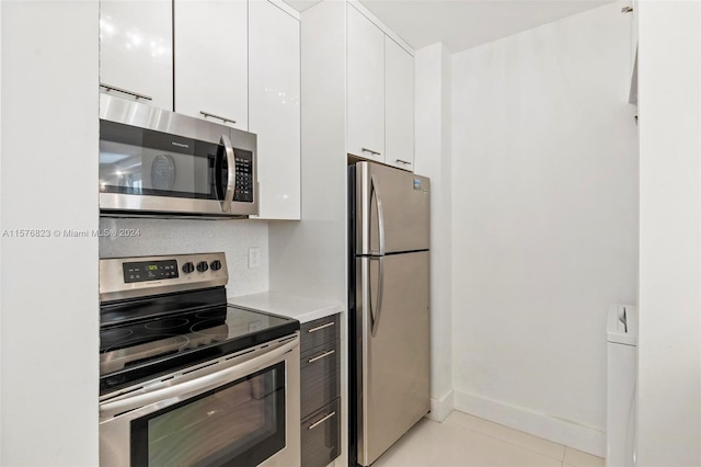 kitchen with washer / dryer, stainless steel appliances, white cabinets, and light tile floors