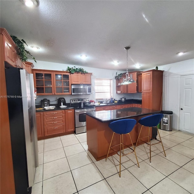 kitchen with appliances with stainless steel finishes, a kitchen bar, light tile floors, and a kitchen island