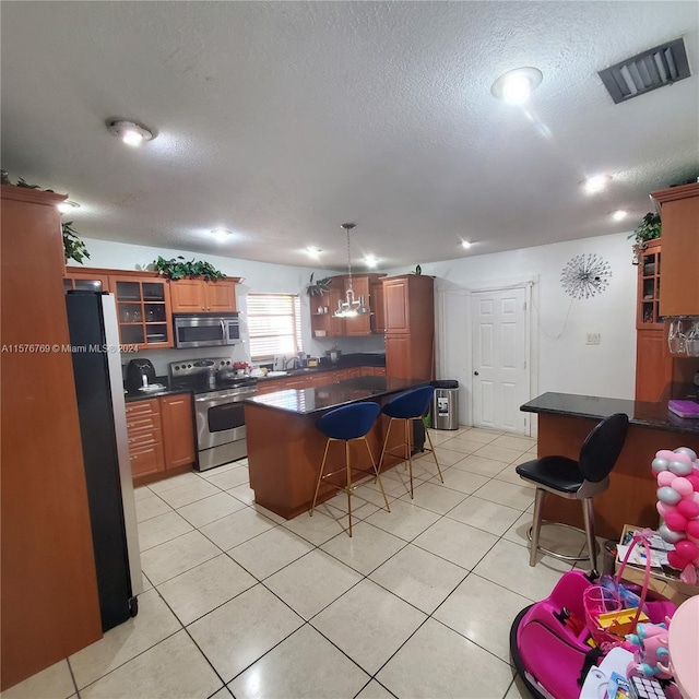 kitchen featuring a kitchen breakfast bar, a kitchen island, appliances with stainless steel finishes, pendant lighting, and light tile floors