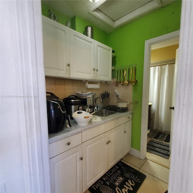 kitchen with backsplash, sink, light tile floors, and white cabinets