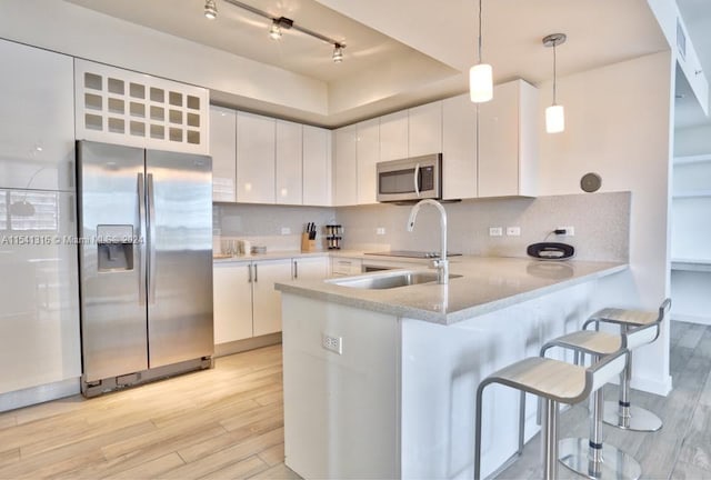 kitchen featuring tasteful backsplash, light wood-type flooring, white cabinetry, stainless steel appliances, and pendant lighting