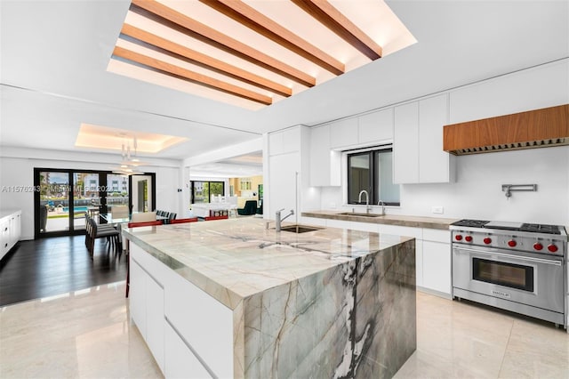 kitchen featuring luxury stove, white cabinetry, a center island with sink, and modern cabinets