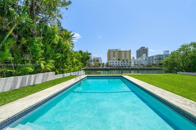 view of swimming pool featuring a city view, a water view, fence, a lawn, and a fenced in pool