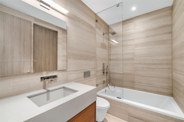 bathroom with tile walls, tiled shower / bath, toilet, and vanity