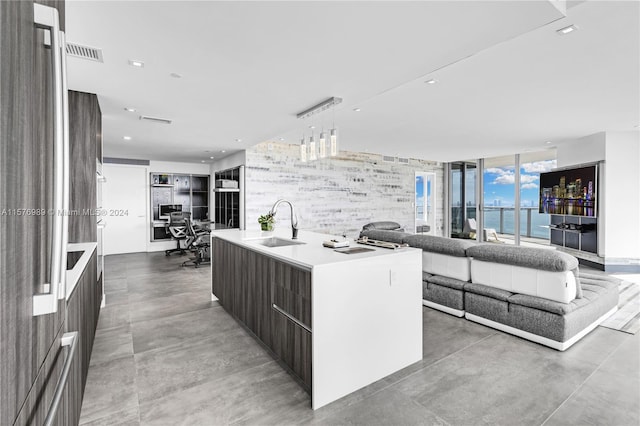 kitchen featuring dark brown cabinetry, a water view, sink, decorative light fixtures, and a kitchen island with sink