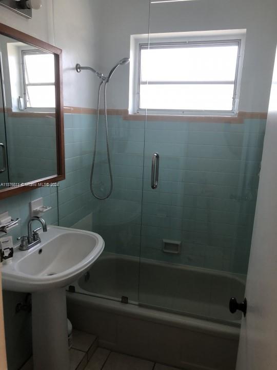 bathroom with shower / bath combination with glass door, a healthy amount of sunlight, and tile walls