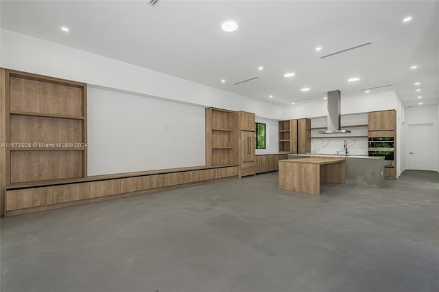 kitchen with wall chimney exhaust hood, a center island, concrete floors, and backsplash