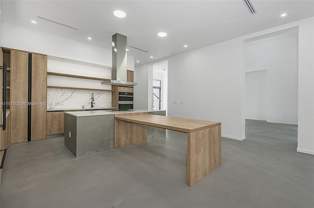 kitchen with a center island, double oven, backsplash, sink, and island exhaust hood