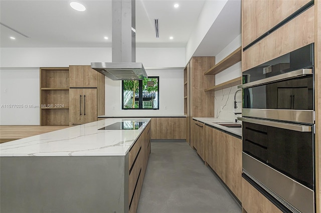 kitchen with black electric stovetop, island range hood, light stone counters, a kitchen island, and stainless steel double oven