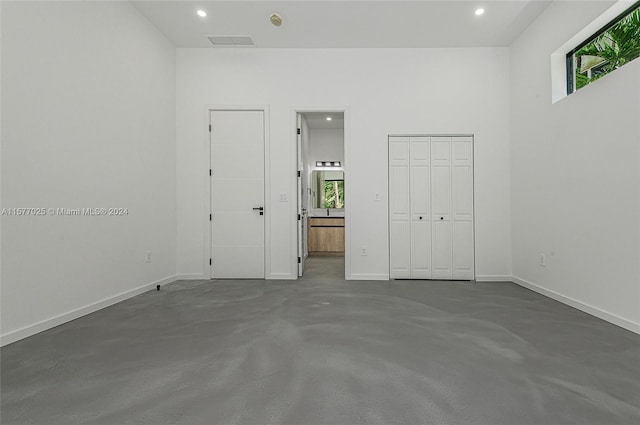 unfurnished bedroom featuring a closet, multiple windows, concrete floors, and ensuite bathroom