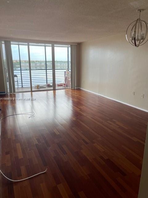 empty room featuring a notable chandelier, expansive windows, a healthy amount of sunlight, and hardwood / wood-style flooring