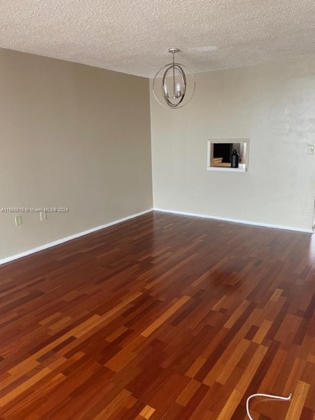 empty room featuring an inviting chandelier, dark hardwood / wood-style floors, and a textured ceiling