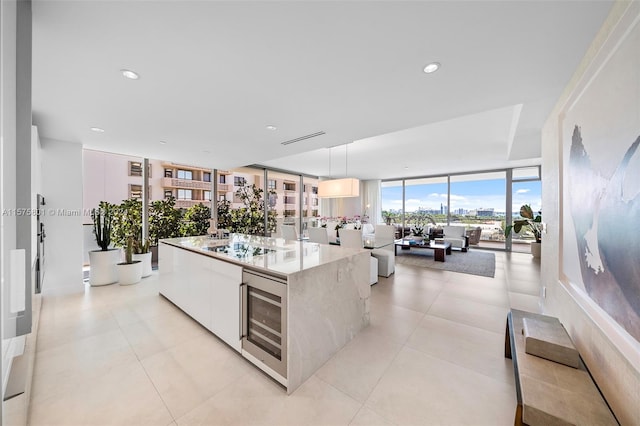 kitchen featuring wine cooler, white cabinetry, decorative light fixtures, expansive windows, and a kitchen island with sink