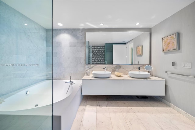 bathroom featuring tasteful backsplash, a bath to relax in, double vanity, and tile walls