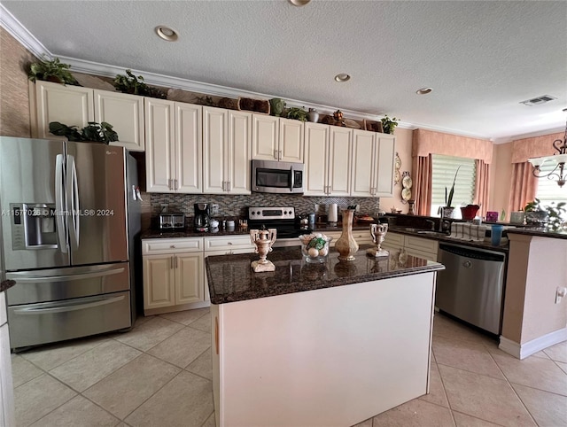 kitchen with appliances with stainless steel finishes, light tile floors, a kitchen island, ornamental molding, and dark stone countertops