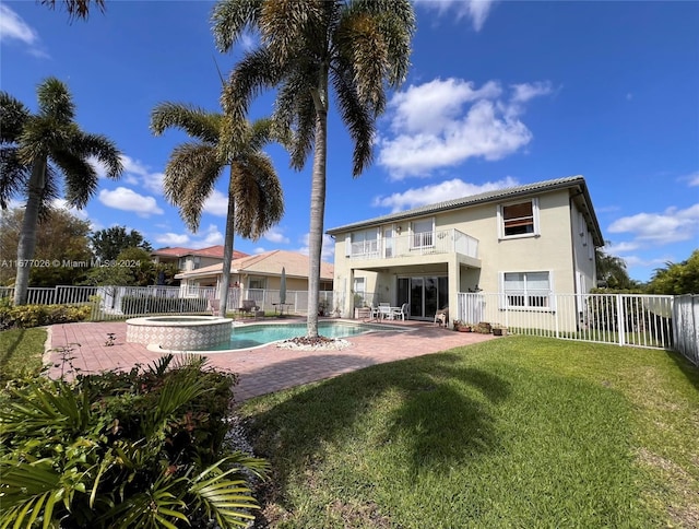 back of property featuring a patio, a balcony, a lawn, and a swimming pool with hot tub