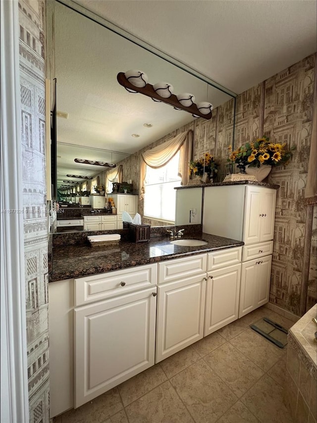 kitchen with sink, dark stone countertops, white cabinets, and light tile floors