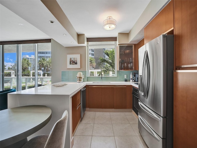 kitchen with stainless steel appliances, kitchen peninsula, sink, light tile patterned floors, and backsplash