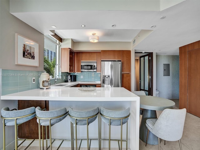 kitchen featuring kitchen peninsula, appliances with stainless steel finishes, sink, decorative backsplash, and a kitchen bar