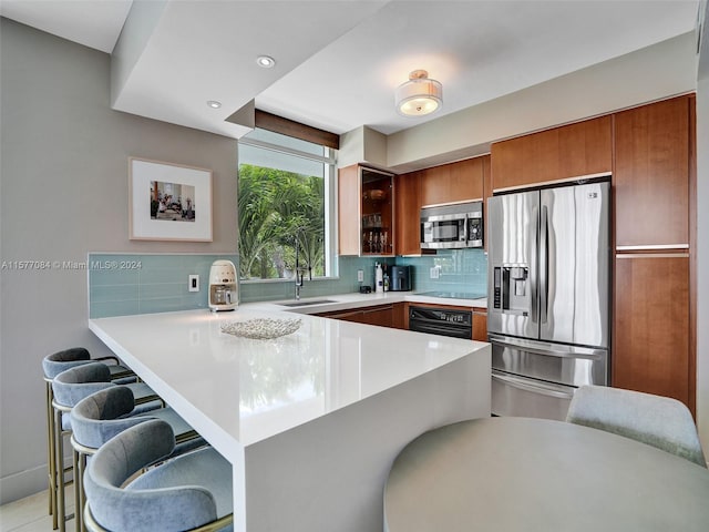 kitchen with kitchen peninsula, a kitchen bar, stainless steel appliances, decorative backsplash, and sink