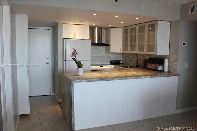 kitchen with stove, a sink, wall chimney range hood, freestanding refrigerator, and tile patterned floors