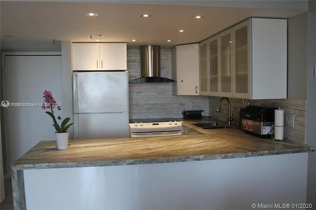 kitchen featuring range with electric stovetop, a sink, wall chimney range hood, freestanding refrigerator, and glass insert cabinets