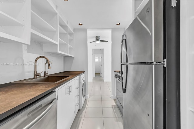 kitchen with white cabinets, sink, light tile patterned flooring, washer / dryer, and stainless steel appliances