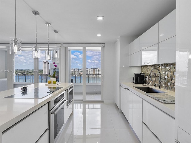 kitchen featuring black electric stovetop, a water view, white cabinetry, oven, and sink