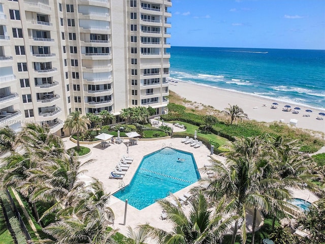 view of swimming pool featuring a water view, a patio area, and a beach view