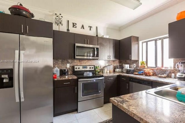 kitchen featuring stainless steel appliances, ornamental molding, dark brown cabinetry, light tile patterned floors, and backsplash