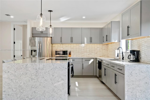 kitchen with backsplash, stainless steel appliances, sink, pendant lighting, and light wood-type flooring