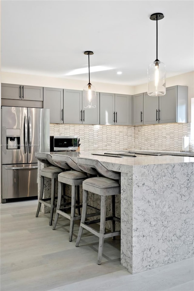 kitchen featuring decorative light fixtures, light hardwood / wood-style floors, tasteful backsplash, stainless steel fridge, and gray cabinetry