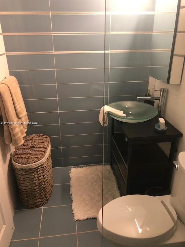 bathroom featuring tile flooring, vanity, toilet, and tile walls