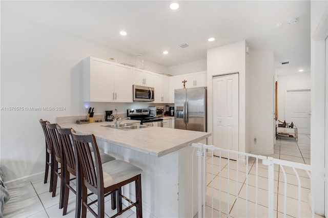 kitchen featuring sink, kitchen peninsula, a breakfast bar area, white cabinetry, and stainless steel appliances